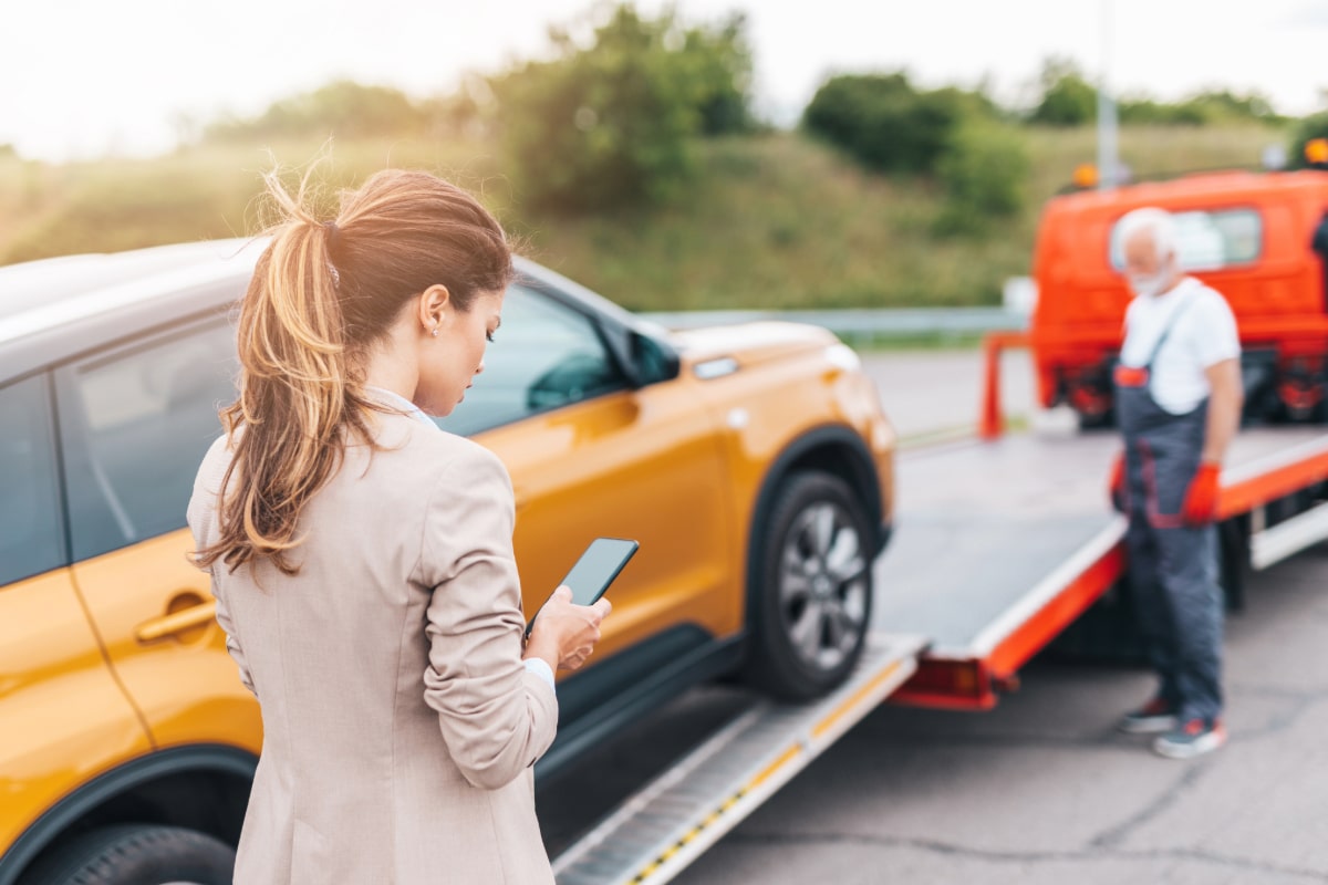 zu sehen ist ein Frau, die auf ihr Handy schaut und ein Mann, der ein Auto abschleppt